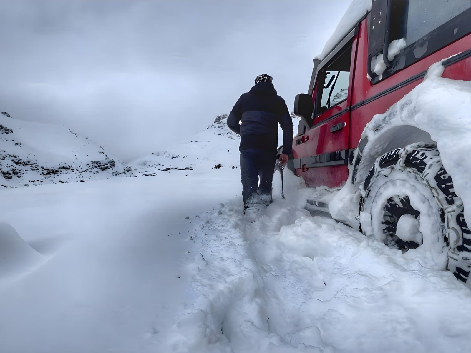 Dinesh wading through deep snow to his snow-chained red Thar on a winter Himalayan expedition
